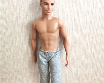 Puede incluir: Un muñeco masculino con el pelo corto rubio que lleva pantalones cortos deportivos grises.