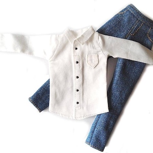 May include: A miniature white button-down shirt with a small pocket and black buttons, paired with blue denim pants. The shirt has long sleeves and a collar. The denim pants have visible stitching.