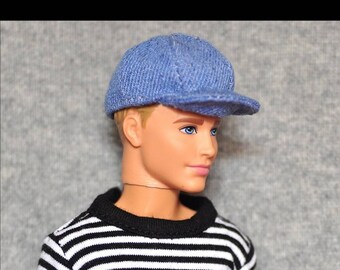 Puede incluir: Una muñeca con una gorra de béisbol de mezclilla azul y una camisa a rayas blancas y negras.
