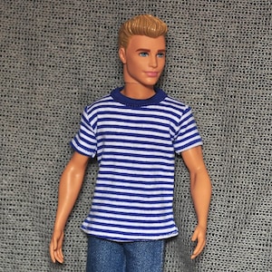 Può includere: Una bambola con una maglietta a righe blu e bianche e jeans blu.