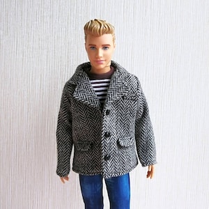 May include: A doll wearing a black and white herringbone patterned jacket with a brown collar and blue jeans.