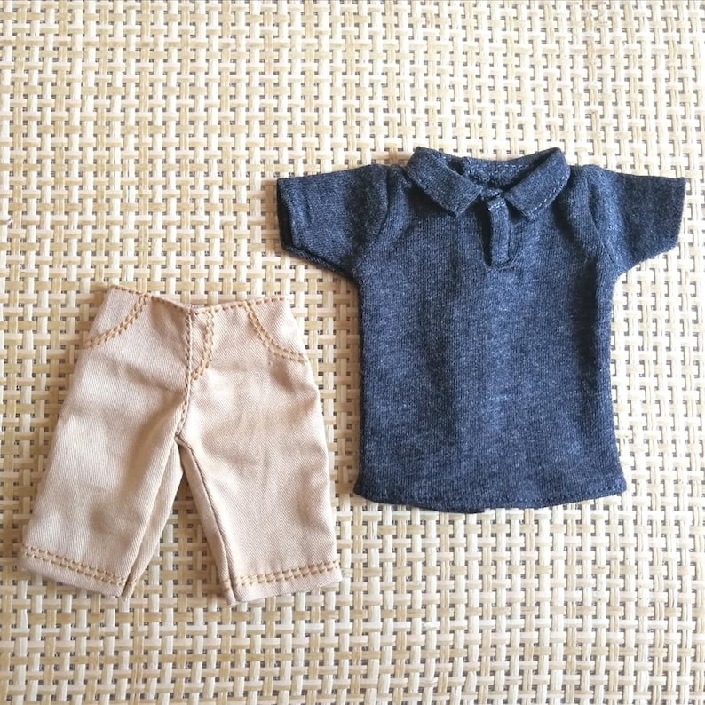 May include: A set of two doll clothes, a tan pair of shorts and a dark gray polo shirt.