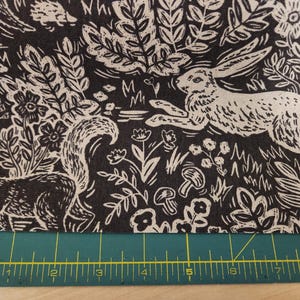 May include: Black and white fabric with a repeating pattern of woodland animals, including a rabbit, squirrel, and mushrooms. The fabric has a vintage, hand-drawn style.