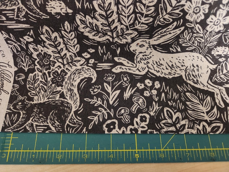 May include: Black and white fabric with a repeating pattern of woodland animals, including a rabbit, squirrel, and mushrooms. The fabric has a vintage, hand-drawn style.