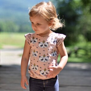 May include: A young girl wearing a pink and white panda print short-sleeved shirt with a blue denim skirt.