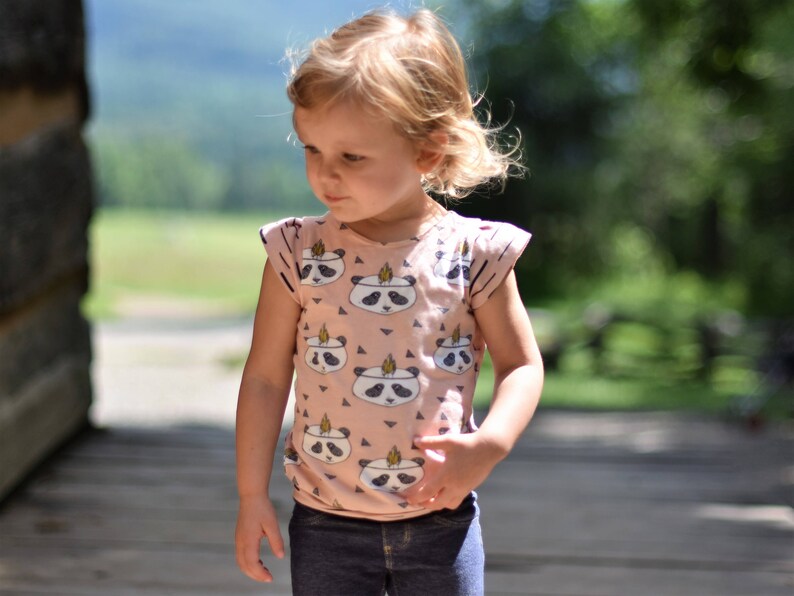 May include: A young girl wearing a pink and white panda print short-sleeved shirt with a blue denim skirt.