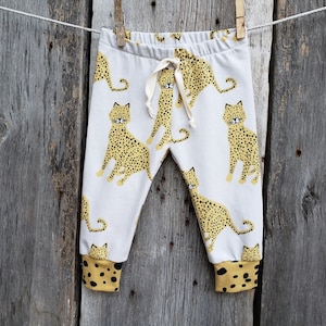 May include: White baby leggings with a cheetah print pattern. The leggings have a drawstring waist and a cuffed hem.