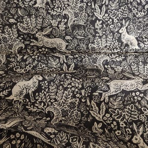 May include: Black and white fabric with a repeating pattern of stylized rabbits, squirrels, and floral designs. The fabric has a vintage, woodblock print aesthetic.