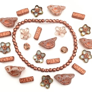 May include: A collection of copper and glass beads, including small flower and bird charms. The beads are arranged in a circle around a strand of copper beads.