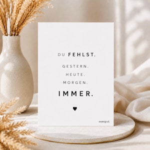 Könnte beinhalten: Eine weiße, rechteckige Grußkarte mit schwarzem Text: DU FEHLST. GESTERN. HEUTE. MORGEN. IMMER. Ein kleines schwarzes Herz-Symbol ist unter dem Text zentriert, und das Wort seelengruß ist in der unteren rechten Ecke aufgedruckt.