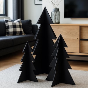 Könnte beinhalten: Vier schwarze, stilisierte Weihnachtsbaumdekorationen in verschiedenen Größen. Die Bäume bestehen aus einem festen Material und haben eine matte Oberfläche. Sie sind auf einem hellgrauen Teppich vor einem Sofa und einem Holzschrank angeordnet.