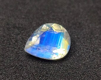 May include: A pear-shaped moonstone gemstone with a blue and white iridescent sheen.