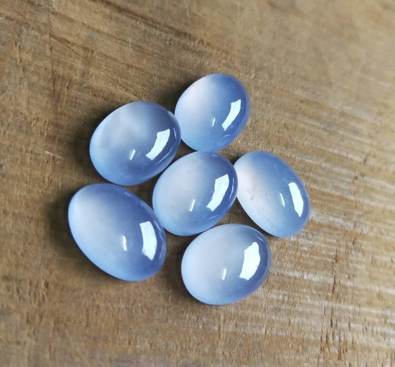 Może przedstawiać: Sześć owalnych, jasnoniebieskich kamieni szlachetnych o gładkim, wypolerowanym wykończeniu. Kamienie szlachetne są ułożone w grupie na drewnianej powierzchni.