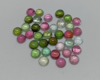 May include: A collection of small, round, cabochon-cut gemstones in various shades of pink, green, and clear white. These polished stones feature smooth, domed surfaces and exhibit a range of translucent and opaque color variations throughout the group.