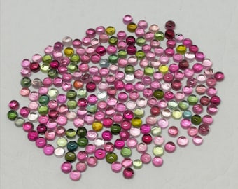May include: A collection of small, round gemstones in various colors, including pink, green, yellow, and red. The gemstones are scattered across a light-colored surface, showcasing their polished, cabochon cut. These gemstones are ideal for jewelry making.