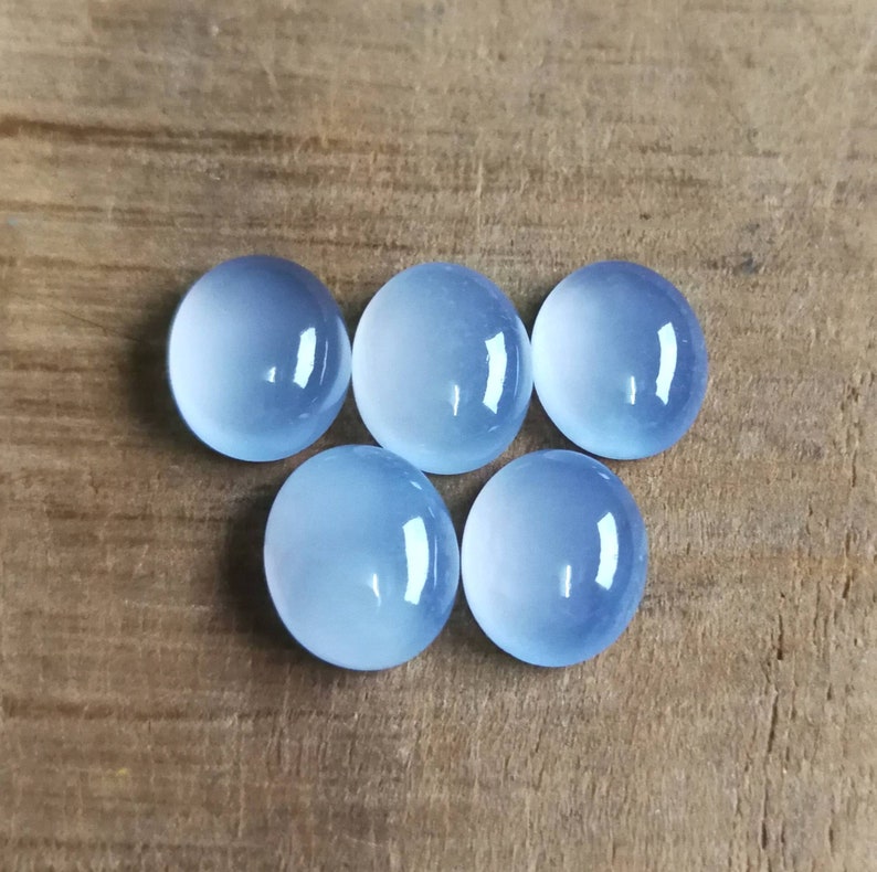 Może przedstawiać: Sześć okrągłych, jasnoniebieskich kamieni szlachetnych w szlifie kaboszonowym na drewnianej powierzchni.