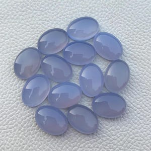 May include: A collection of 14 oval-shaped, light blue chalcedony gemstones. The stones are smooth and polished, with a translucent appearance.