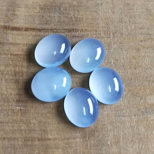 Może przedstawiać: Pięć owalnych, jasnoniebieskich kamieni szlachetnych w formie kaboszon&oacute;w na drewnianej powierzchni.