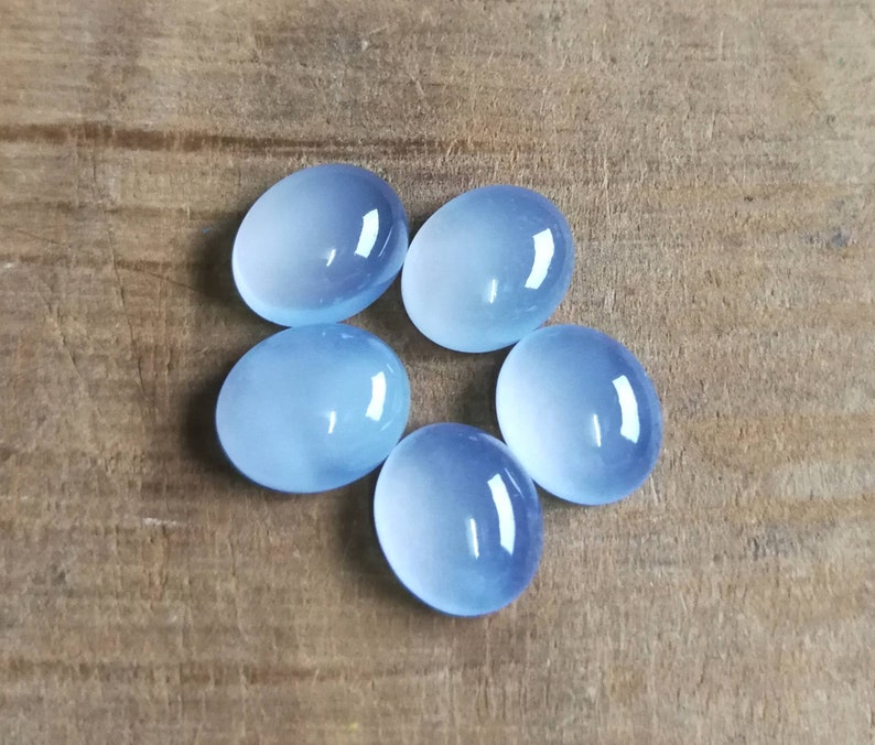 Może przedstawiać: Pięć owalnych, jasnoniebieskich kamieni szlachetnych w formie kaboszon&oacute;w na drewnianej powierzchni.