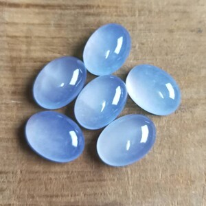 Może przedstawiać: Sześć owalnych, jasnoniebieskich kamieni szlachetnych o gładkim, wypolerowanym wykończeniu. Kamienie są ułożone w grupie na drewnianej powierzchni.