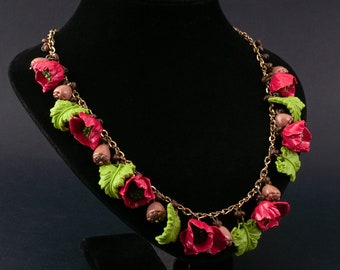 Peut inclure: Un collier rouge et vert avec des breloques de fleurs et de glands. Le collier est fait d'une chaîne dorée et est présenté sur un mannequin noir.