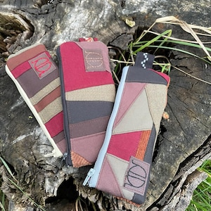 Può includere: Tre pochette con cerniera realizzate in tessuto patchwork in tonalità di marrone, rosso e beige. Ogni pochette ha una chiusura a cerniera e un piccolo logo ricamato.