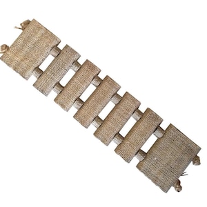 May include: A rectangular, natural-toned burlap table runner with a ladder-like design. The runner features rectangular panels connected by shorter, horizontal strips. Small, decorative knots are at each end.