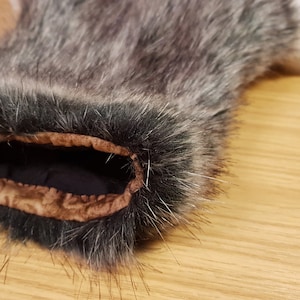 K&ouml;nnte beinhalten: Nahaufnahme des Innenbereichs einer grauen und schwarzen Kunstfellmanschette. Die Manschette hat ein braunes Stofffutter mit einem dekorativen Muster.