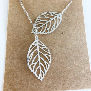 May include: A silver necklace with two delicate leaf pendants. The leaves are cut out with a detailed design and hang from a thin silver chain.