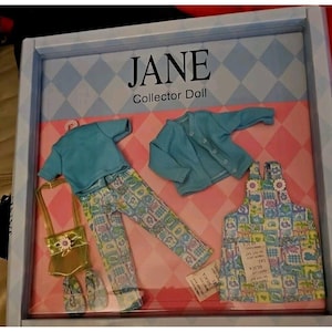 May include: A doll outfit set in a blue and green color scheme. The set includes a blue cardigan, a blue t-shirt, patterned pants, a patterned overall dress, a yellow purse, and a pair of shoes. The set is packaged in a box with the words "JANE Collector Doll" printed on it.