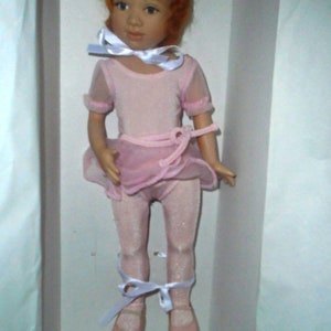 May include: A porcelain doll wearing a pink ballerina costume with white ribbons. The doll has red hair and blue eyes.