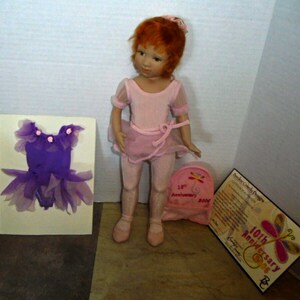 May include: A porcelain doll with red hair wearing a pink leotard and tutu. The doll is holding a pink bag with a butterfly design and the text "10th Anniversary 2006". The doll is also wearing pink ballet shoes. The doll is accompanied by a purple tutu and a certificate.