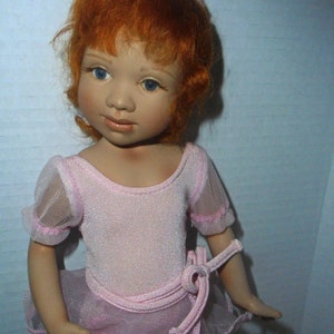 May include: A porcelain doll with red hair wearing a pink leotard and a tulle skirt.