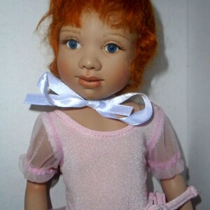 May include: A porcelain doll with red hair wearing a pink leotard and a white ribbon around her neck.