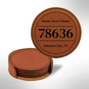 May include: A set of brown leather coasters with the text "Home Sweet Home" and the number "78636" in black. The coasters are round with a stitched border and are stacked in a matching holder. The text "Johnson City, TX" is also visible.