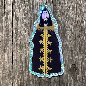 Puede incluir: Una pegatina de un personaje de dibujos animados que lleva una túnica negra con ribetes dorados y una larga barba. El personaje tiene una expresión triste en su rostro.