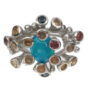 May include: A silver ring with a large blue opal gemstone surrounded by smaller gemstones in various colors, including yellow, red, and blue.