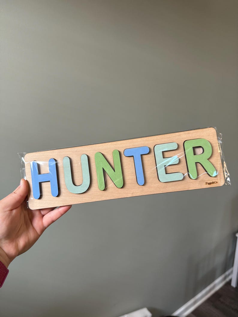 May include: A wooden puzzle with the name "HUNTER" spelled out in colorful letters. The letters are in shades of blue, green, and light blue. The puzzle is made by "PuzzleCo."