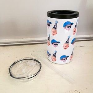 May include: A white stainless steel tumbler with a black lid and a straw. The tumbler is covered in a pattern of a baby's face wearing a blue baseball cap and sunglasses. Some of the baby's faces are wearing a party hat with the number "1/2" on it.