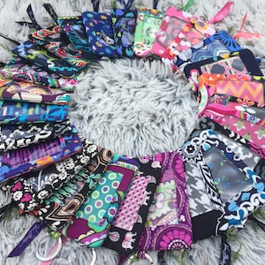 May include: A collection of colorful patterned fabric card holders with clear plastic windows. The holders are arranged in a circle on a fluffy white surface.