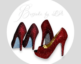 May include: Three pairs of red sparkly high heel shoes. The shoes have a peep toe and a platform. The shoes are decorated with rhinestones. The shoes are on a white background. Bespoke by LA is written in cursive at the top of the image.