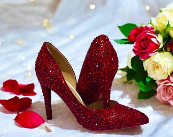 May include: A pair of red high-heeled shoes covered in sparkling rhinestones. The shoes are pointed-toe and have a thin stiletto heel.