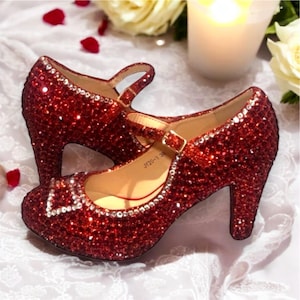 May include: A pair of red sparkly high-heeled shoes with a buckle strap. The shoes are covered in rhinestones and have a pointed toe.