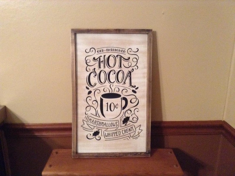 May include: A rectangular wooden sign with a distressed white finish and a dark brown frame. The sign features black text that reads OLD-FASHIONED HOT COCOA, MARSHMALLOWS, and WHIPPED CREAM, along with a graphic of a mug labelled 10 cents.