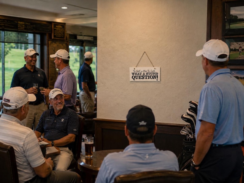 May include: A rectangular white wooden sign hanging on a wall with black text that reads: To Golf or Not To Golf... WHAT A STUPID QUESTION! The sign is suspended by a thin piece of twine and features small black star accents above the text.