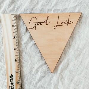 May include: A wooden triangle sign with the words "Good Luck" written in cursive on it.