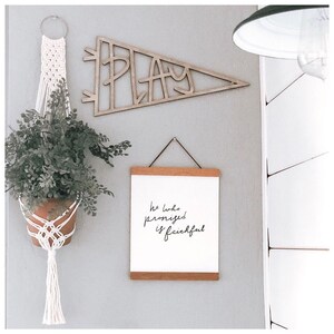 Pu&ograve; includere: Un cartello in legno per la decorazione murale con la parola "PLAY" a forma di pennone. Una stampa incorniciata con il testo "He who promised is faithful" &egrave; appesa sotto il cartello. Una pianta in vaso &egrave; appesa a un portavasi in macram&egrave;.