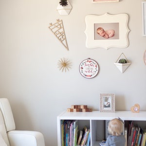 Pu&ograve; includere: Una libreria bianca con libri, coperte e un cesto. Un bambino &egrave; in piedi davanti alla libreria, guardando i libri. La parete dietro la libreria &egrave; decorata con una variet&agrave; di immagini incorniciate, tra cui una foto di un bambino, una foto di una pianta e un cartello che dice "hello".