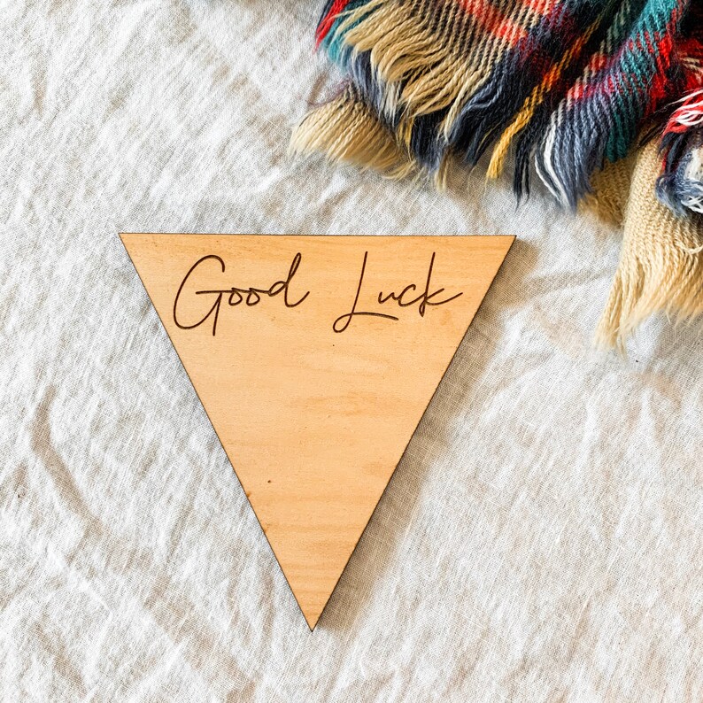 May include: A triangular wooden sign with the words "Good Luck" engraved in cursive.