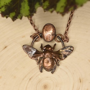 May include: A copper necklace with a bee pendant and a copper circle. The bee is detailed with wings and a body.